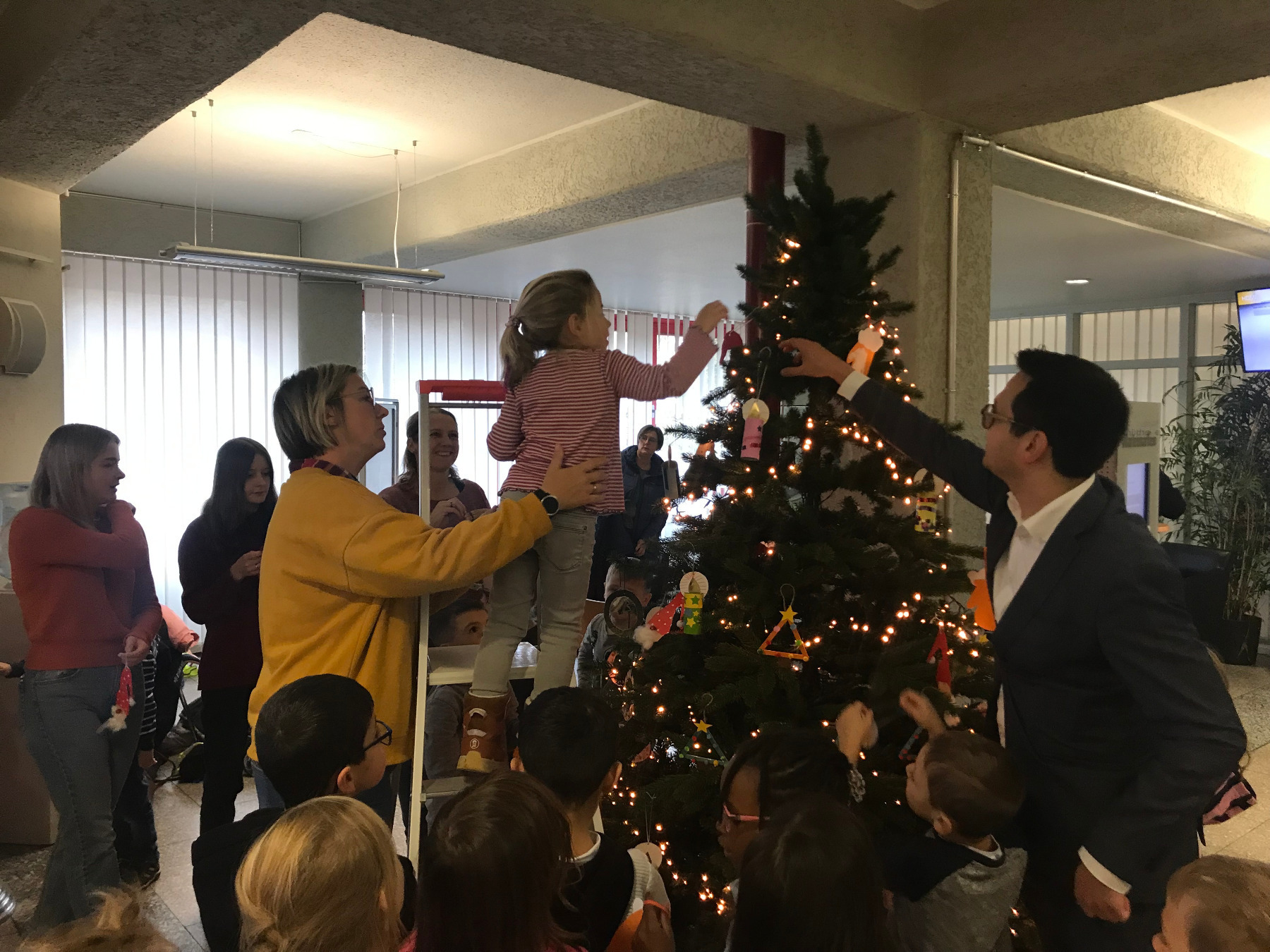 Herzogenraths Bürgermeister Dr. Benjamin Fadavian und Kinder der Kita Lydia-Gemeinde schmücken den Weihnachtsbaum im Herzogenrather Rathausfoyer