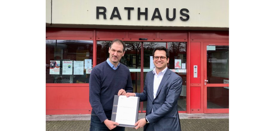 Franz-Josef Türck-Hövener, Technischer Beigeordneter der Stadt Herzogenrath (links im Bild), und Bürgermeister Dr. Benjamin Fadavian (rechts im Bild) präsentieren den Zuwendungsbescheid (mittig) vor dem Herzogenrather Rathaus.