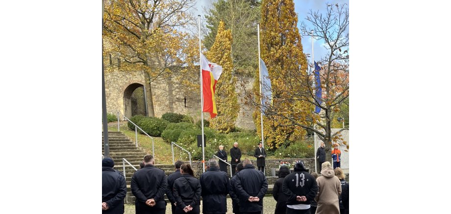 Herzogenraths Bürgermeister Dr. Benjamin Fadavian mit der Bürgermeisterin Kerkrades und dem Pastoralreferanten bei der Gedenkveranstaltung in Herzogenrath-Mitte an der Burg Rode, Flaggen auf Halbmast im Hintergrund