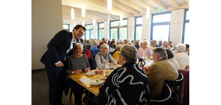 Abgebildet sind Herzogenraths Bürgermeister Dr. Benjamin Fadavian und Teilnehmer der Seniorenfahrt nach Inden: Der Bürgermeister besuchte die Senioren, als diese gerade im Restaurant aßen. Die Menschen auf dem Bild lachen