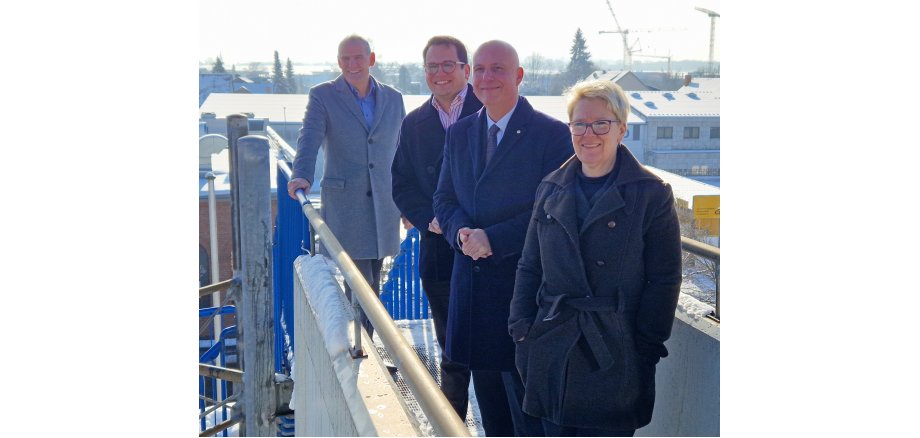 Vertreterinnen und Vertreter von Stadt Herzogenrath und Stadtentwicklung (vlnr.: Stadtkämmerer und Erster Beigeordneter Hubert Philippengracht, Bürgermeister Dr. Benjamin Fadavian, Geschäftsführer der SEH und der Technologie-Park Herzogenrath GmbH Michael Eßers und SEH-Projektmanagerin Ulrike Greiner-Lövenich); im Hintergrund das zu bebauende Grundstück. 