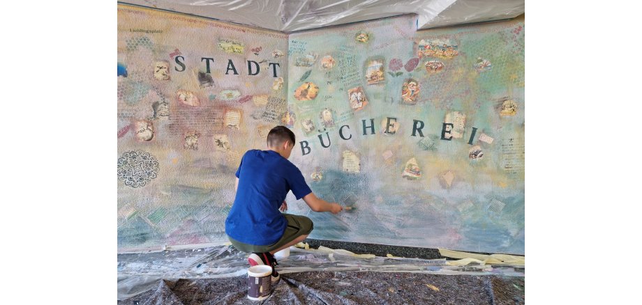 Ein Jugendlicher gestaltet die Wand in der Stadtbibliothek mit verschiedenen Farben und Gestaltungselementen