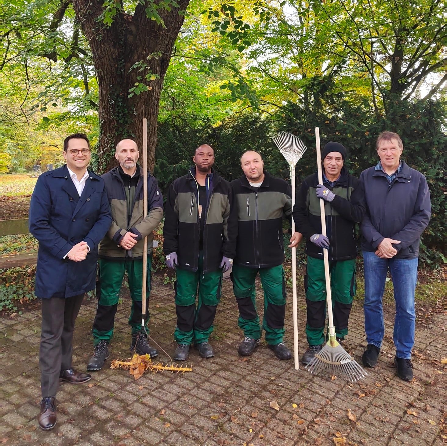 Gruppenbild der Geflüchteten im Einsatz mit Dr. Benjamin Fadavian (li.) und Rainer Schulte, Abteilungsleiter des Bereichs Grünflächen/Friedhöfe/Baubetrieb