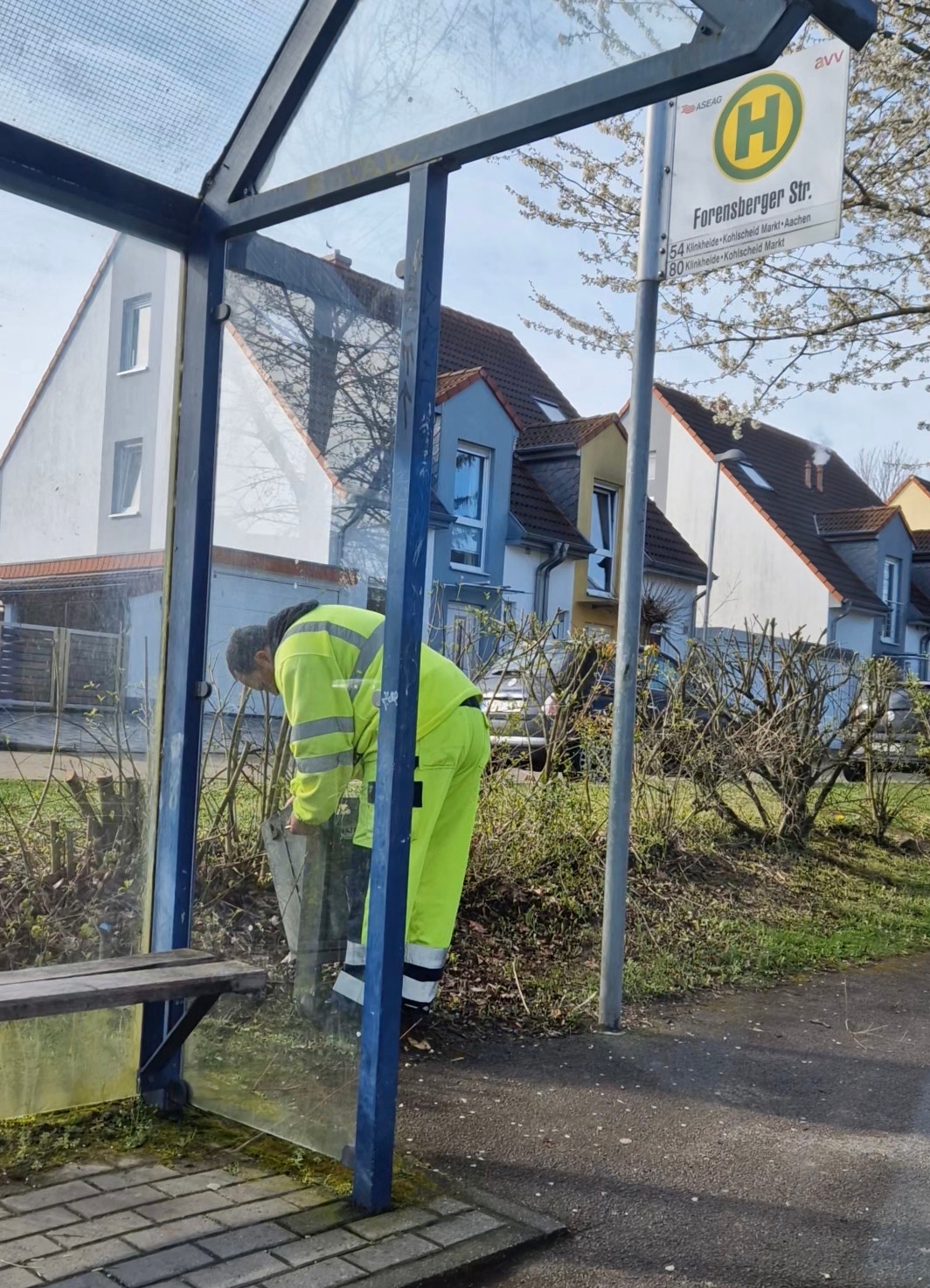 Ein Mitarbeiter des Bauhofs leert einen öffentlichen Mülleimer an einer Bushaltestelle in Herzogenrath