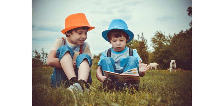 Zwei Jungen lesen draußen an der frischen Luft im Gras ein Buch