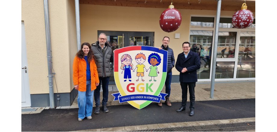 Das Gruppenbild zeigt v.l.n.r. Schulleiterin Heike Keller, Markus Müller als Vorsitzender des Ausschusses für Bildung und Schulbauangelegenheiten, den Technischen Beigeordneten Franz-Josef Türck-Hövener und Bürgermeister Dr. Benjamin Fadavian mit dem neuen Schullogo.