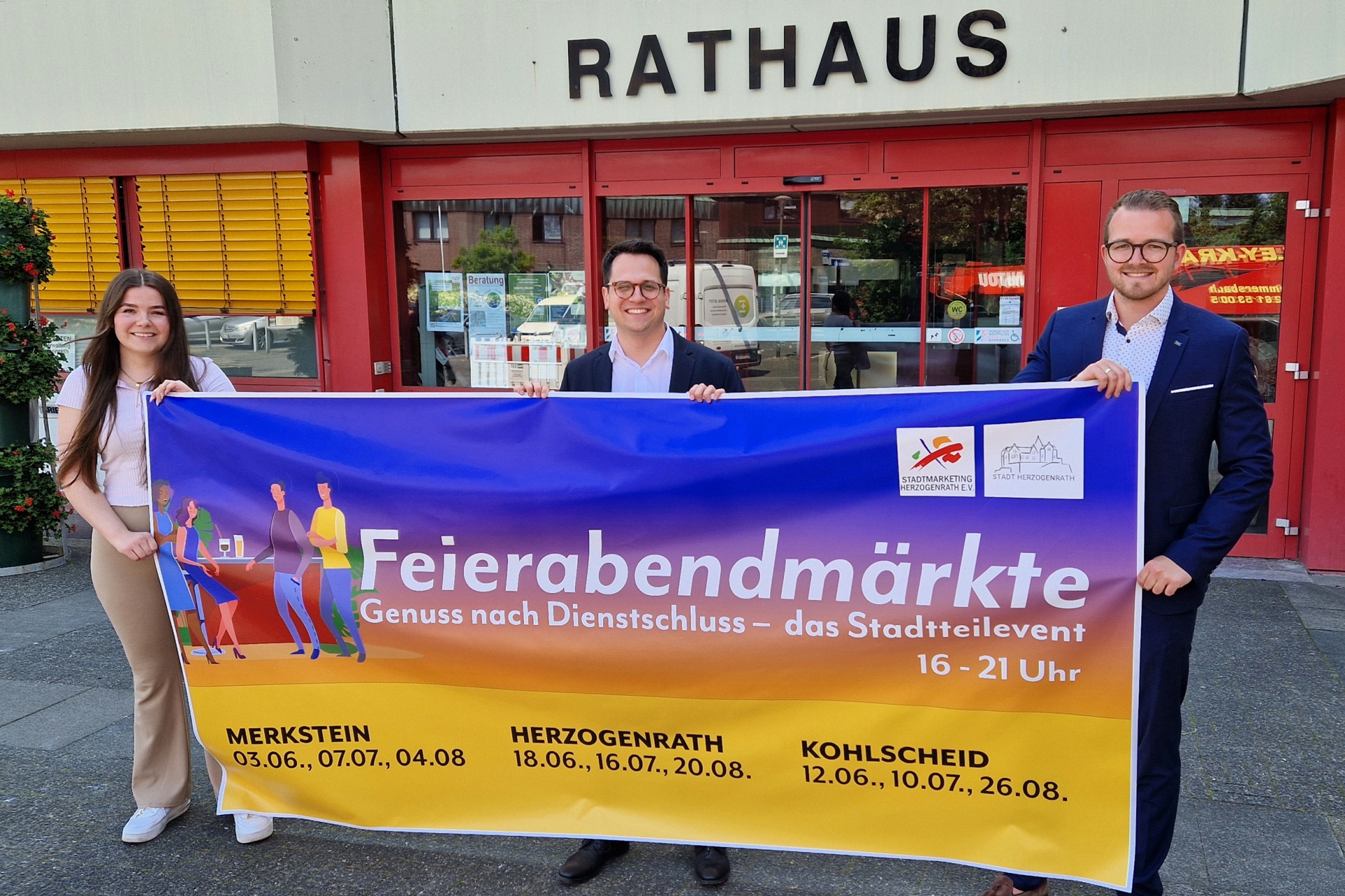 Das Bild zeigt v.l.n.r. Emily Nievelstein (Geschäftsführerin Stadtmarketing Herzogenrath e.V.), Bürgermeister Dr. Benjamin Fadavian und Yannick Wimmers (Büroleiter Bürgermeisterbüro) mit dem Ankündigungsbanner für die diesjährigen Feierabendmärkte