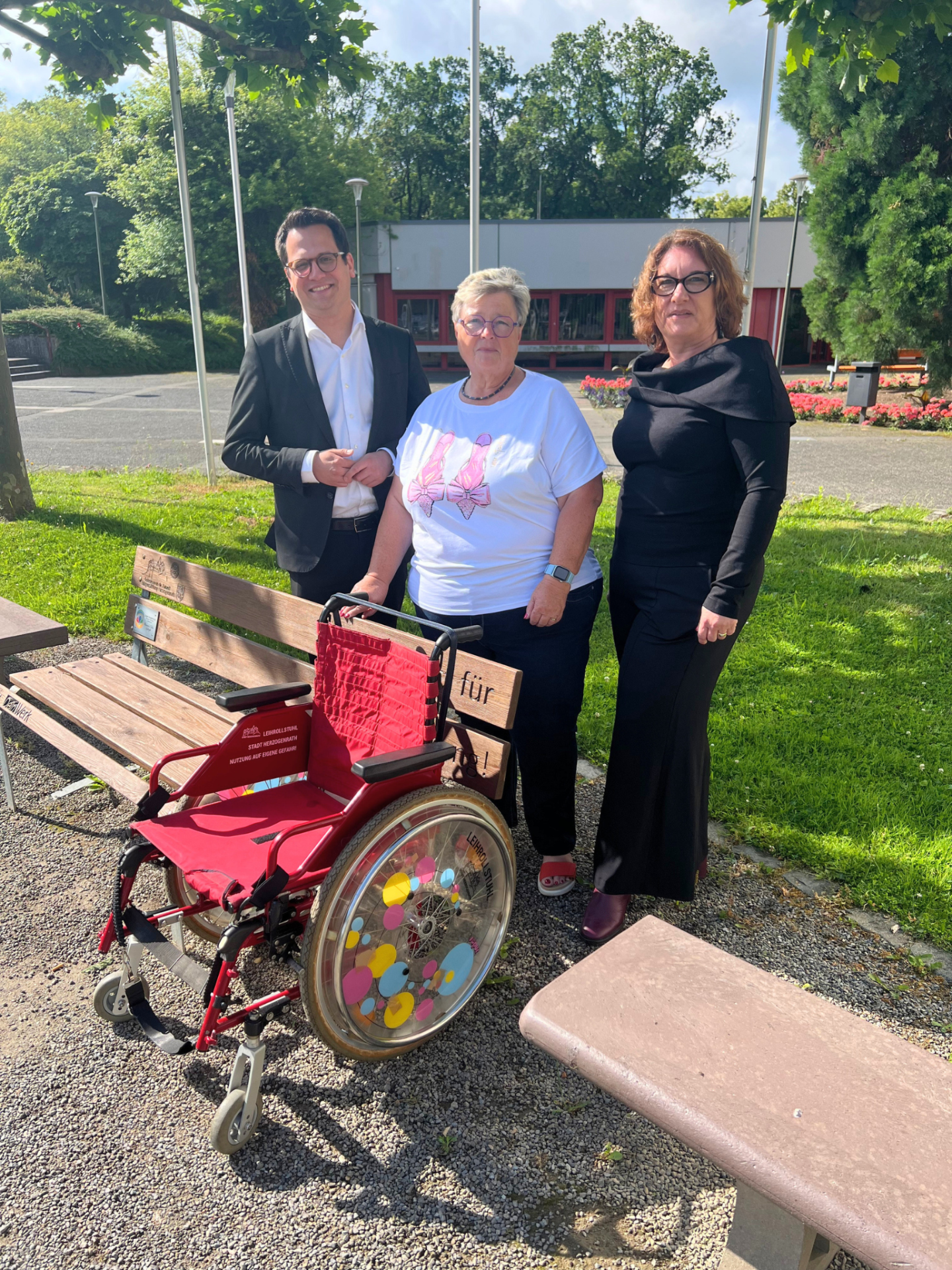 Das Bild anbei zeigt den neuen Rollstuhl mit (v.l.n.r.) Bürgermeister Dr. Benjamin Fadavian, Karin Rana vom Forum für Menschen mit Behinderung und der Beigeordneten Renate Wallraff an der Sitzbank „Kein Platz für Ausgrenzung“ vor dem Herzogenrather Rathaus.