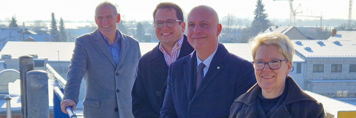 Vertreterinnen und Vertreter von Stadt Herzogenrath und Stadtentwicklung (vlnr.: Stadtkämmerer und Erster Beigeordneter Hubert Philippengracht, Bürgermeister Dr. Benjamin Fadavian, Geschäftsführer der SEH und der Technologie-Park Herzogenrath GmbH Michael Eßers und SEH-Projektmanagerin Ulrike Greiner-Lövenich); im Hintergrund das zu bebauende Grundstück. 